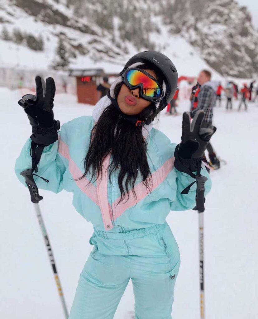 A young woman posing in front of a snowy mountain in Andorra, in a very retro powder blue and dusty pink ski jumper!