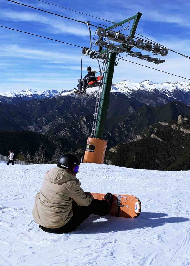 A young man sitting on a snowy mountain in Andorra, taking a break from snowboarding.