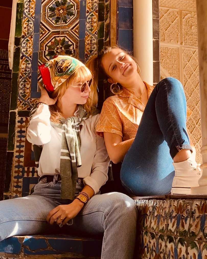 Two young women sitting in front of a beautiful casa wall